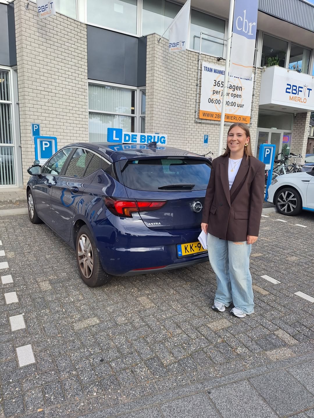Geslaagde leerling poseert naast de lesauto bij het examencentrum
