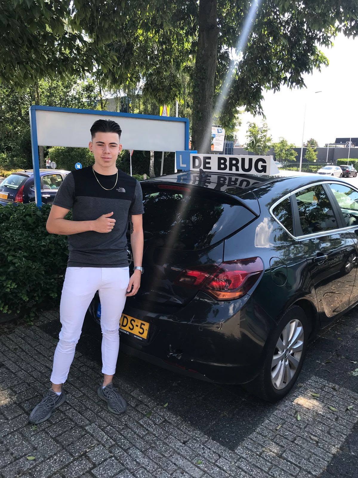 Geslaagde leerling bij de achterkant van de lesauto van Autorijschool De Brug